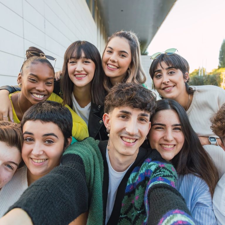 Group of cheerful multiracial friends in casual clothes smiling and looking at camera while sitting on stairs near building